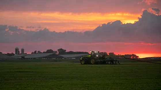 Farmer blading in manure at sunset