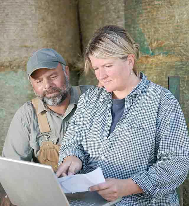 A man and woman looking at papers on a laptop.