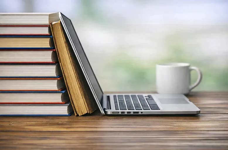 Stack of books with a laptop and coffee mug