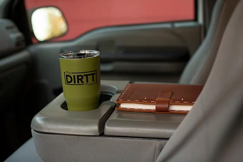 A DIRTT mug and notebook on the armrest in a truck